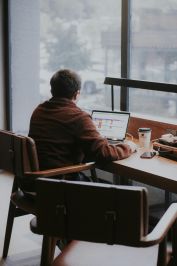 A man is working on a laptop at a café table, creating a warm, productive atmosphere.