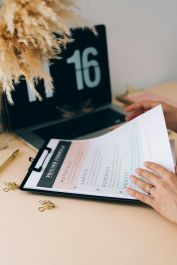 Hands review business documents on clipboard beside a laptop on a desk.