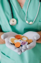 From above crop faceless doctor with stethoscope on shoulders holding in hands chocolate coins