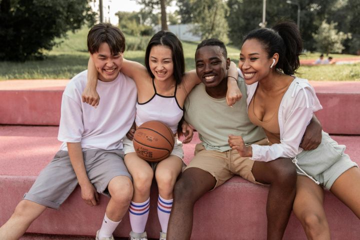 A diverse group of young friends sharing joyful moments outdoors with a basketball.